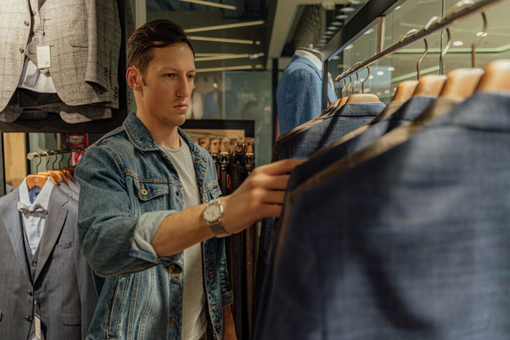 Young man browsing through suits in a retail clothing store, selecting new attire.